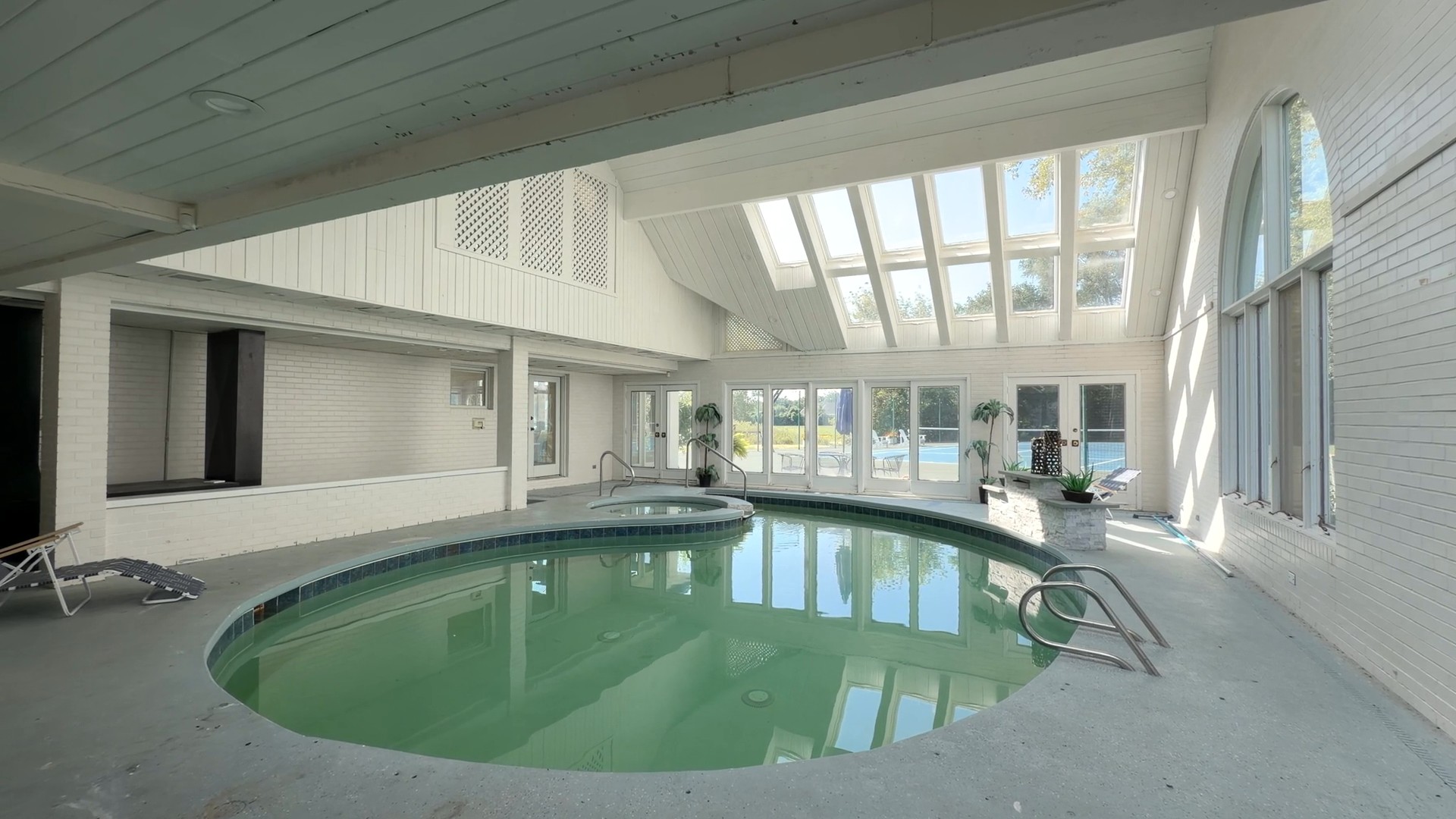 Naperville luxury estate indoor heated swimming pool looking directly through floor-to-ceiling glass out to the private regulation tennis and pickleball court at 23W735 Hobson Rd